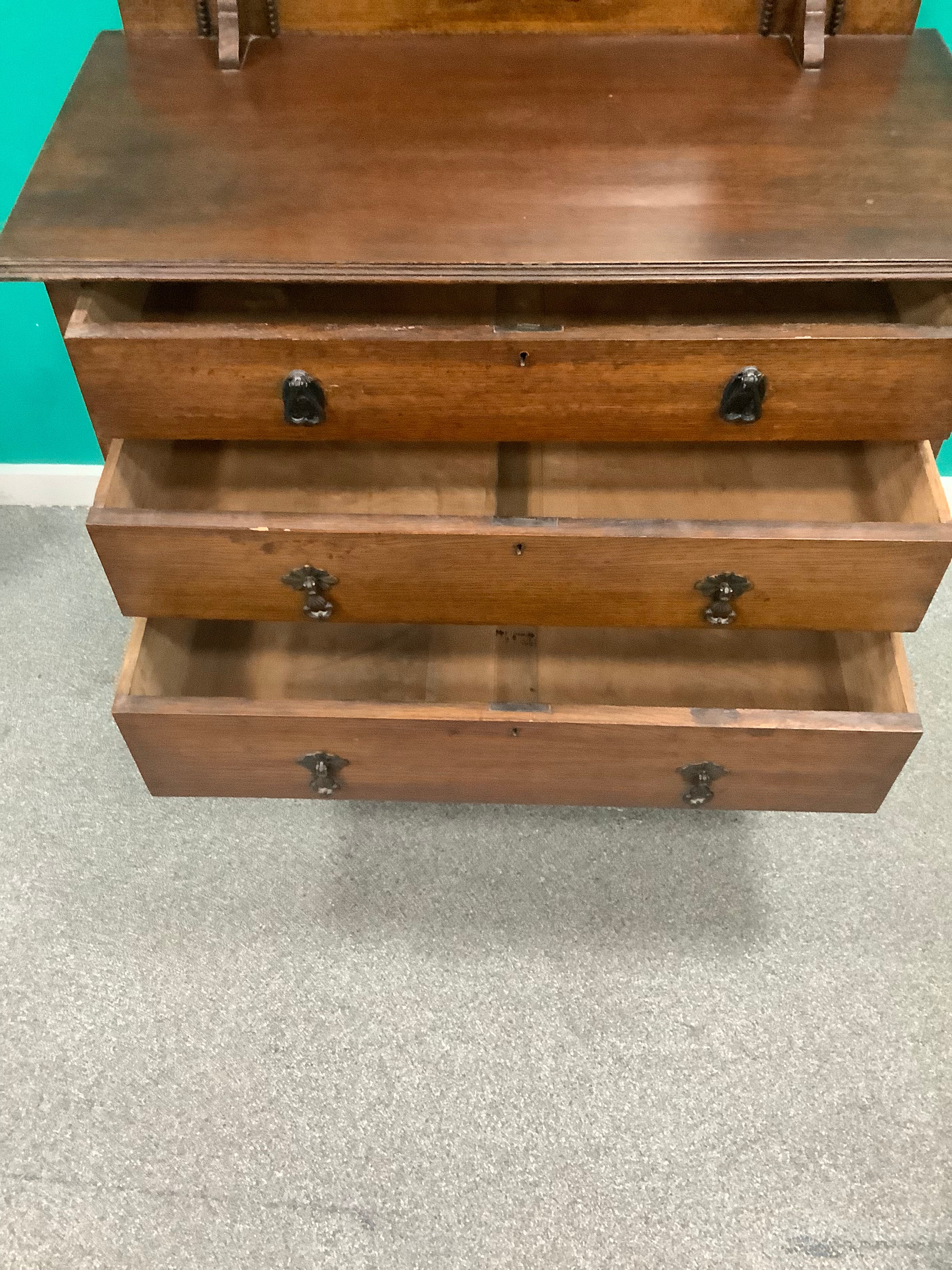 An antique Edwardian Arts & and Crafts dark oak dressing chest featuring a swing vanity mirror, decorative pierced metal drop handles, and a three-drawer configuration. 170826009