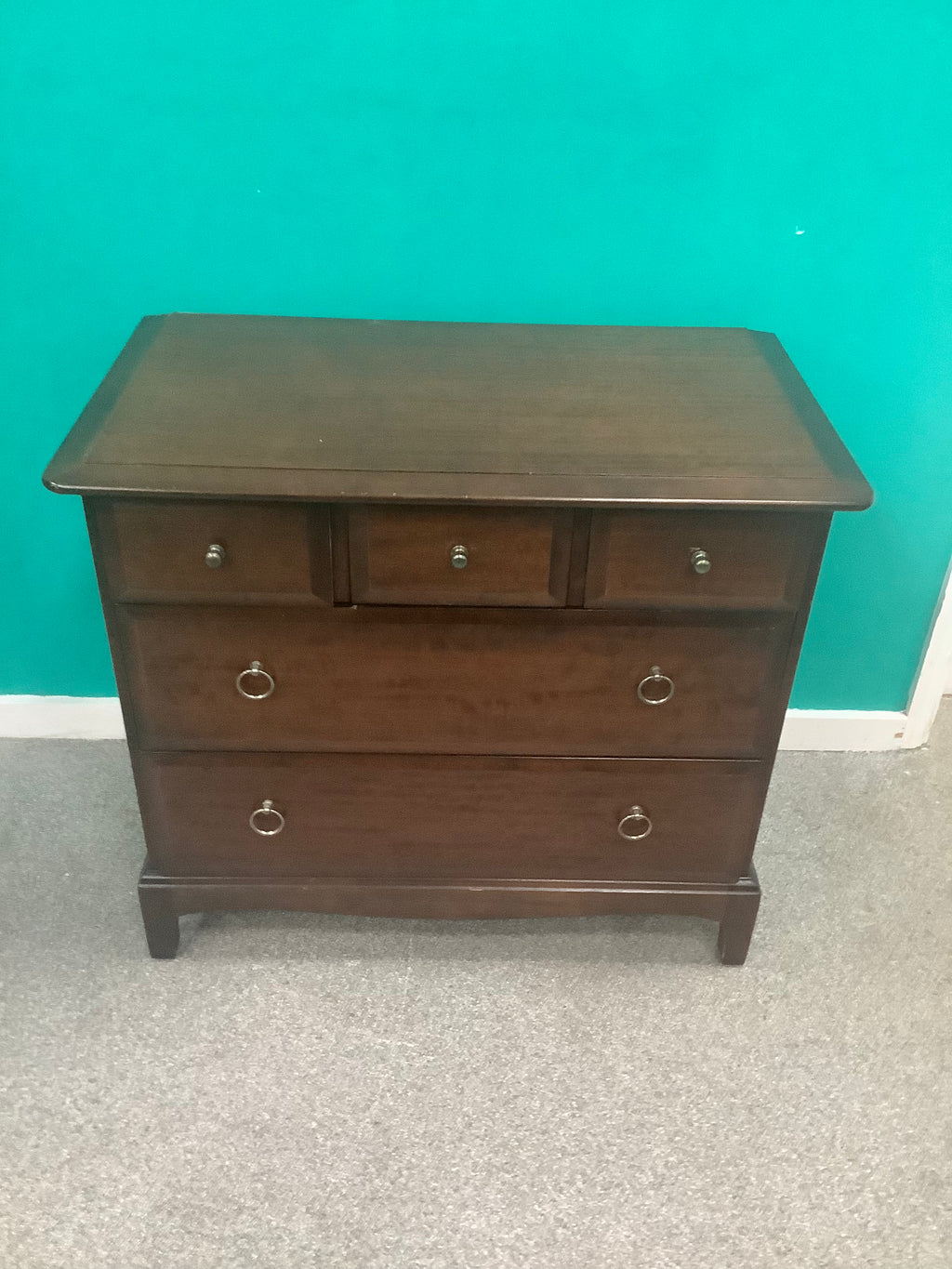 Stag Minstrel 3-over-2 chest of drawers, designed by John & Sylvia Reid in the mid-20th century and crafted from mahogany or cherry veneers with distinctive brass-toned ring pull handles. 190826003