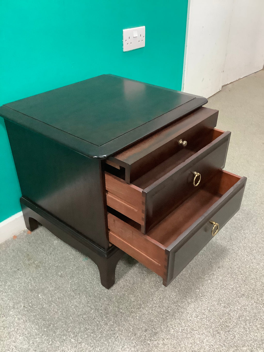 Stag Minstrel mahogany bedside cabinet featuring a pull-out sliding shelf above two drawers with distinctive brass-toned ring pulls. 240826001