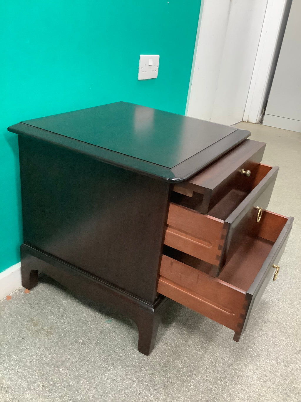 Stag Minstrel mahogany bedside cabinet featuring a pull-out sliding shelf above two drawers with distinctive brass-toned ring pulls. 240826001