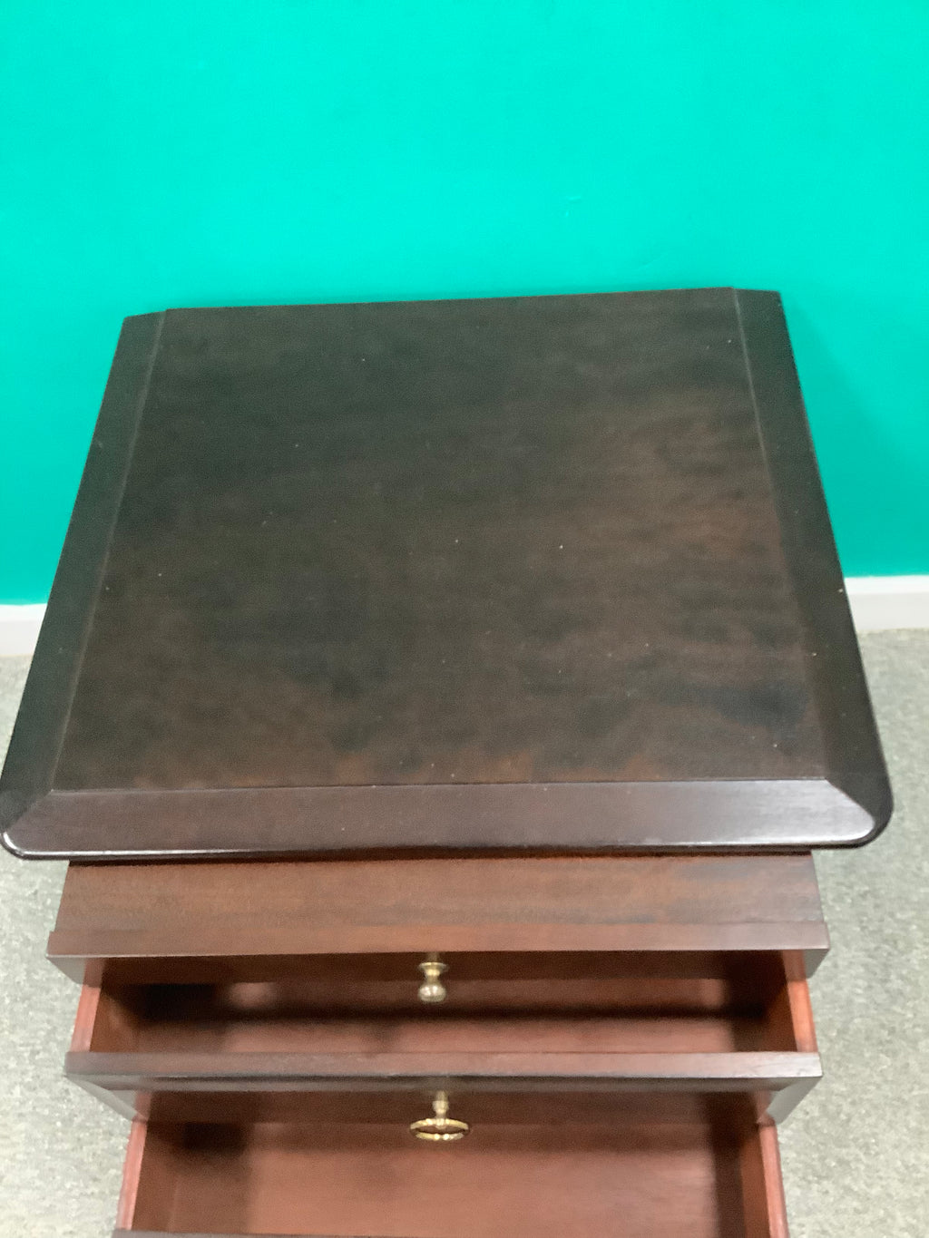 Stag Minstrel mahogany bedside cabinet featuring a pull-out sliding shelf above two drawers with distinctive brass-toned ring pulls. 240826001