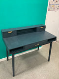 This is the dark blue or charcoal vintage-style "Penelope" 3-drawer desk by Maisons du Monde, featuring distinct brass-finish half-moon handle pulls and an elevated upper tier with integrated small compartments. 240826004